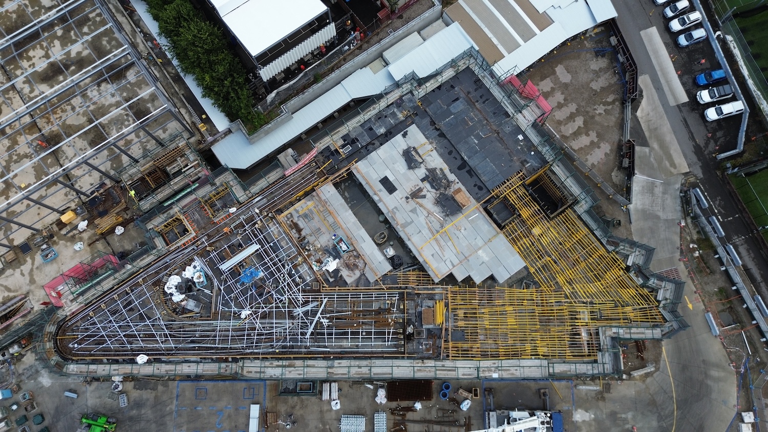 Straight down over a major concrete slab pour in progress. Workers are screeding and finishing wet concrete across a large floor plate, with reinforcing steel bars being prepared for the next section to the right. 