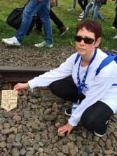 Carol at Auschwitz with a memorial plaque to the Jews of Greece